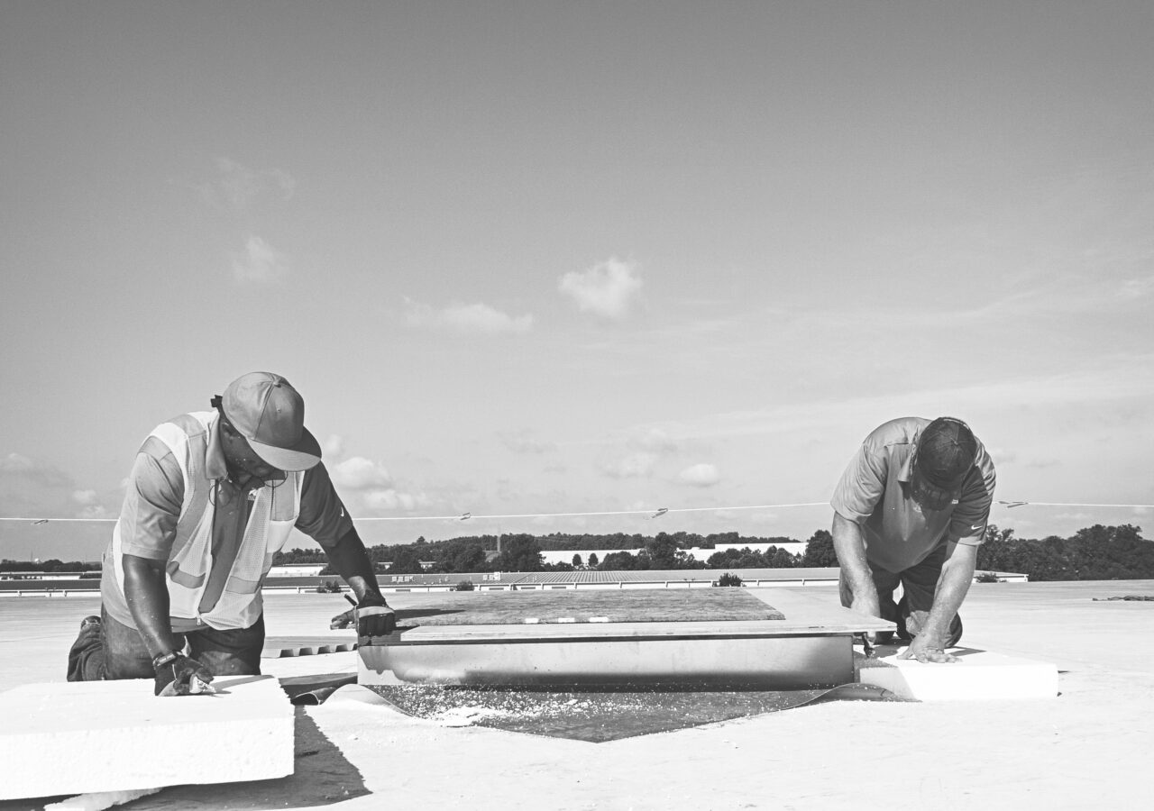 two roofers on top of a flat roof doing maintenance